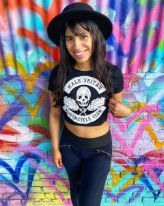 Woman with hat wearing kale seitan motorcycle shirt with skull and kale against graffiti wall
