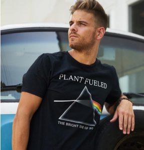 man leaning against vw bus wearing black plant fueled shirt with prism