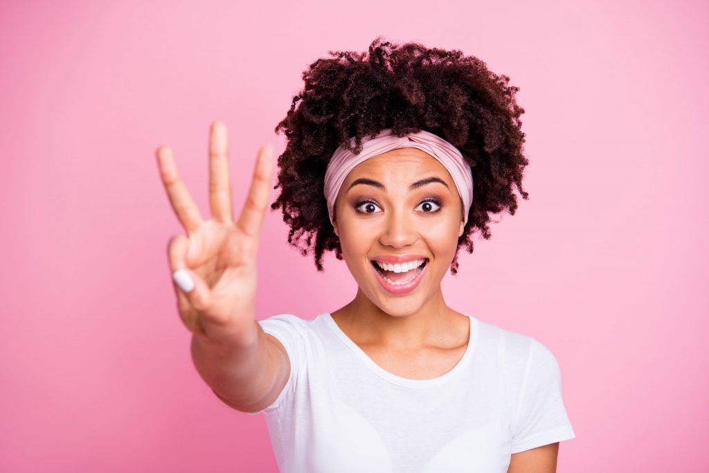 Dark skinned woman with white shirt pink headband holding up middle three fingers