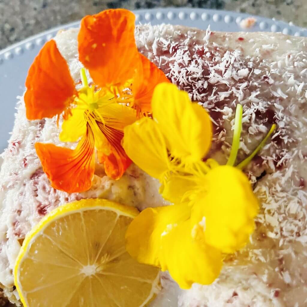 raspberry pineapple marble cake topped with lemon slice coconut and yellow and orange flowers
