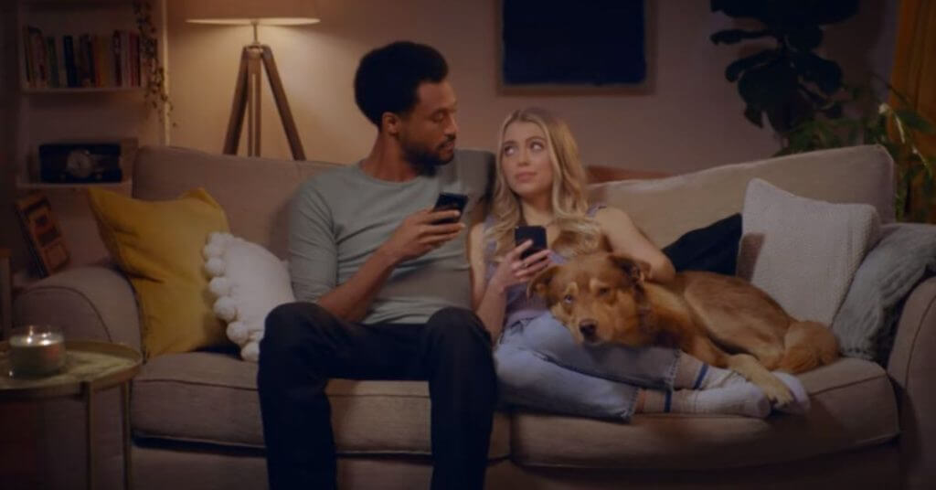 Man and woman sitting on a couch with dogs with cellphones in their hands