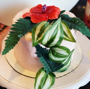 cake decorated with tropical plants a red hibiscus flower ferns and pothos