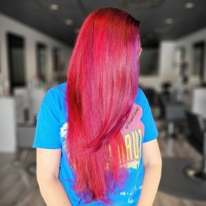 vegan colorist side view of woman with long bright pink red hair and face framing violet highlights
